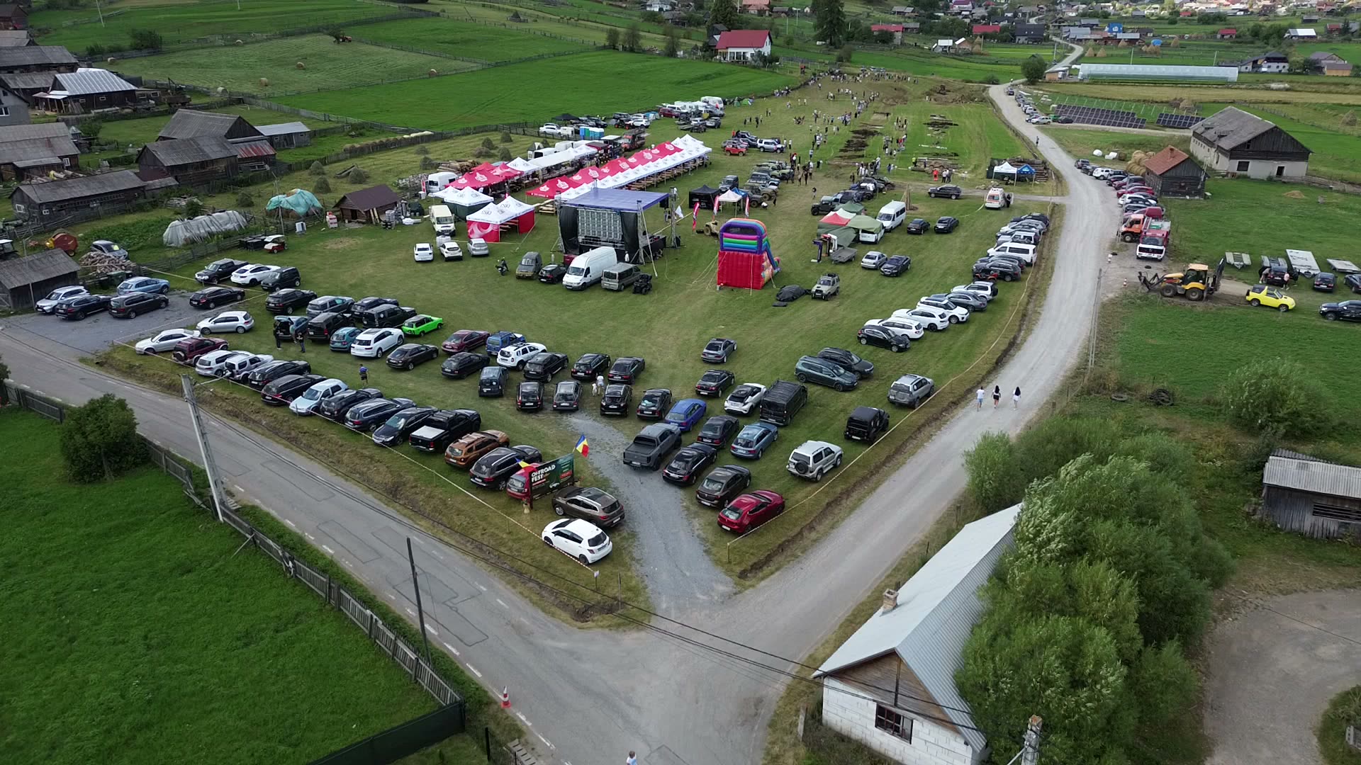 Vedere de sus asupra festivalului de la Bilbor, cu mașinile parcate, corturile și satul în fundal