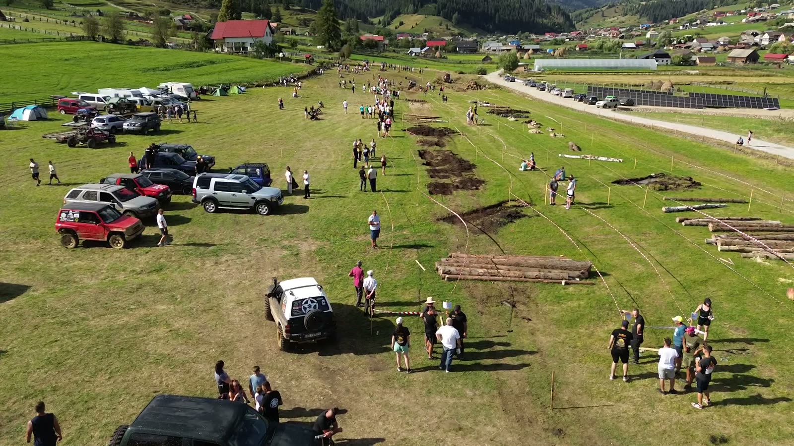 Mașină 4x4 albă la startul pistei de la Bilbor, cu gropi de noroi, bușteni și bandă roșu-albă pe traseu și mașini parcate lângă public